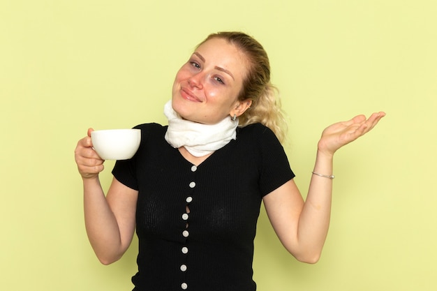 Vorderansicht junge Frau fühlt sich sehr krank und krank lächelnd halten Tasse Kaffee auf hellgrüne Wand Krankheit Medizin Krankheit Gesundheit
