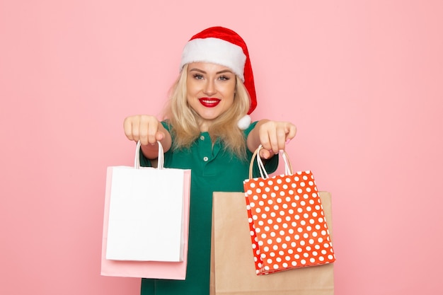 Vorderansicht junge Frau hält Weihnachtsgeschenke in Paketen auf rosa Wandfoto Modell Neujahrsfeiertag