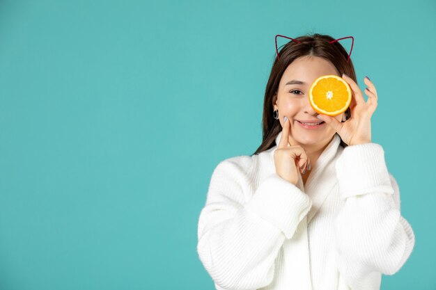 Vorderansicht junge Frau im Bademantel mit Orangenscheibe auf blauem Hintergrund