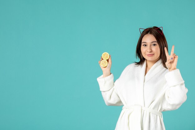 Vorderansicht junge Frau im Bademantel mit Zitronenscheiben auf blauem Hintergrund