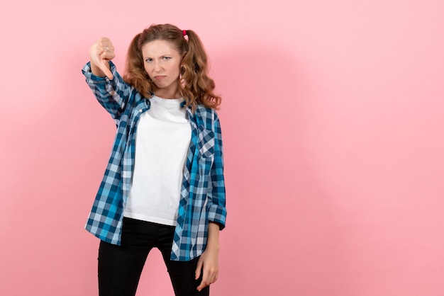 Kostenloses Foto vorderansicht junge frau im blauen karierten hemd, das auf rosa hintergrundemotionsmädchenmodemodelljugendkind aufwirft