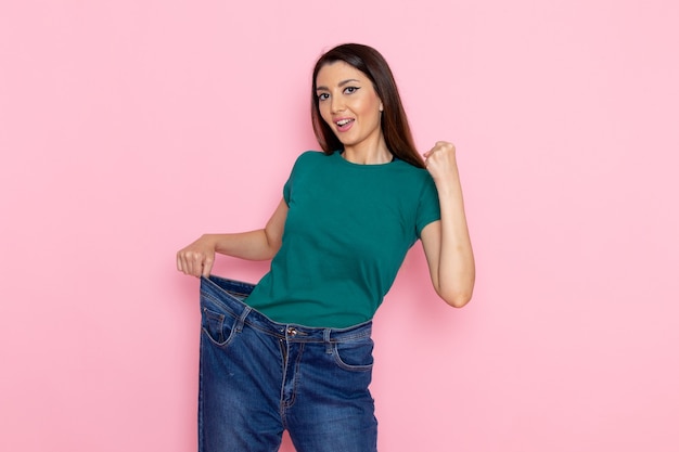 Vorderansicht junge Frau im grünen T-Shirt, die ihre Taille auf der hellrosa Wandtaille Sportübung Workouts Schönheit schlanke Sportlerin prüft