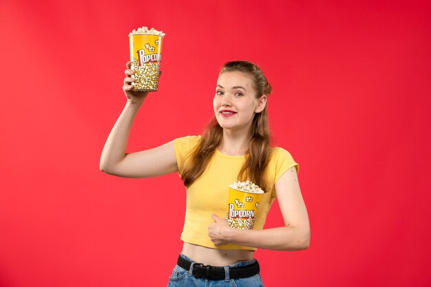 Vorderansicht junge Frau im Kino, die Popcorn auf hellrotem Wandkino der weiblichen Spaßzeitfilm des Kinos hält