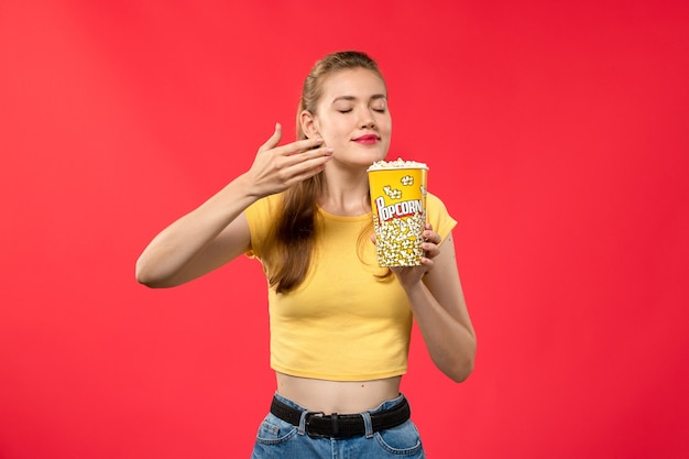 Vorderansicht junge Frau im Kino, die Popcorn-Paket hält und es auf rotem Wandfilmtheaterkino weiblichem Spaßfilm riecht