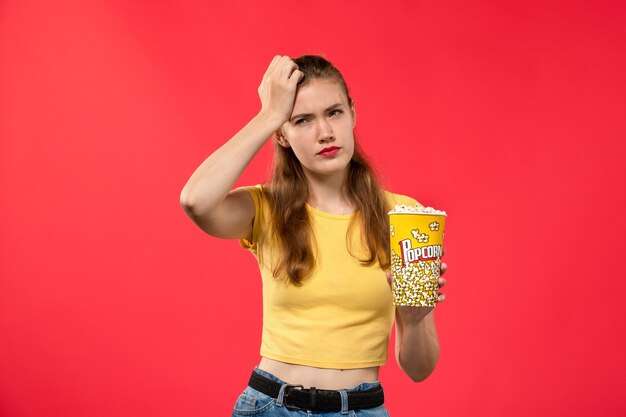 Vorderansicht junge Frau im Kino hält Popcorn-Paket betont auf dem hellroten Wand Kino Kino weiblichen Spaßfilm