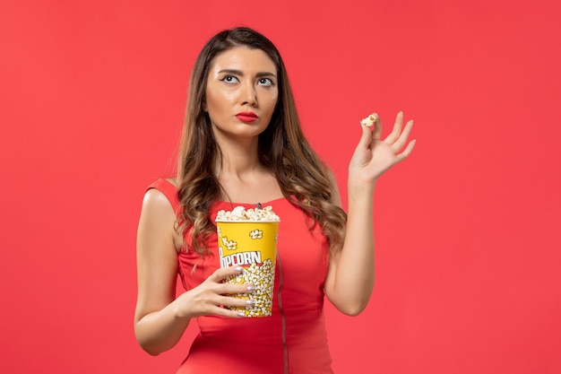 Vorderansicht junge Frau im roten Hemd, das Popcorn auf der roten Oberfläche hält