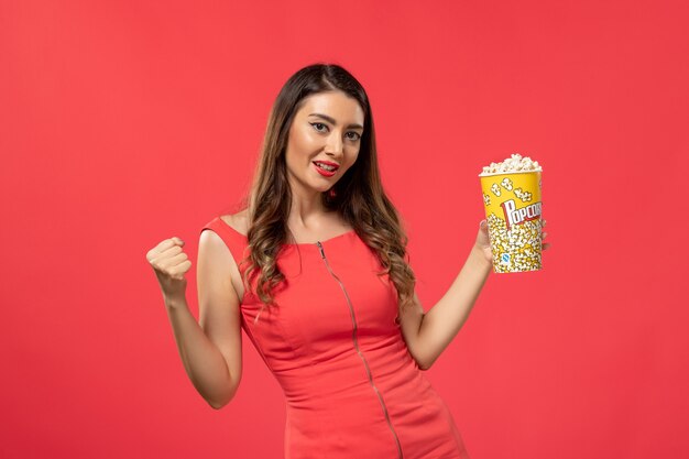 Vorderansicht junge Frau im roten Hemd, das Popcorn auf hellroter Oberfläche hält