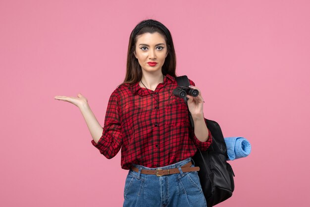 Vorderansicht junge Frau im roten Hemd mit Fernglas auf dem rosa Hintergrundfrauenfarbstudenten