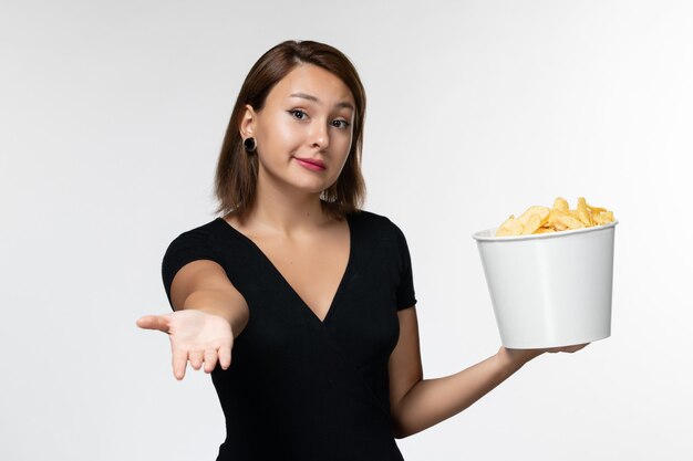 Vorderansicht junge Frau im schwarzen Hemd, das Kartoffelchips auf hellweißer Oberfläche hält