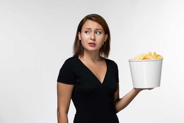 Vorderansicht junge Frau im schwarzen Hemd, das Kartoffelchips auf weißem Schreibtisch hält