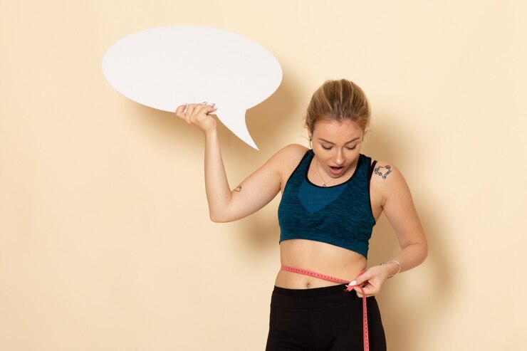 Kostenlose Foto vorderansicht junge frau im sportoutfit, das weißes zeichen hält und ihren körper misst