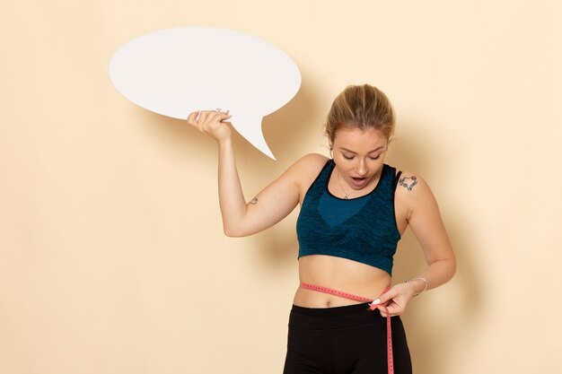 Vorderansicht junge Frau im Sportoutfit, das weißes Zeichen hält und ihren Körper misst