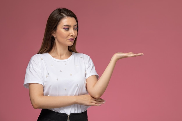 Kostenloses Foto vorderansicht junge frau im weißen hemd, das mit erhabener hand auf der rosa wand aufwirft, farbfrau stellt modellfrau dar