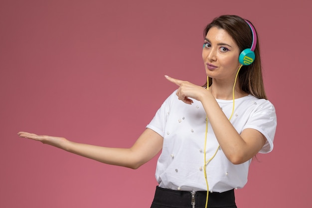 Vorderansicht junge Frau im weißen Hemd, das Musik hört, die auf der rosa Wand lächelt, Farbfrau Modellfrau