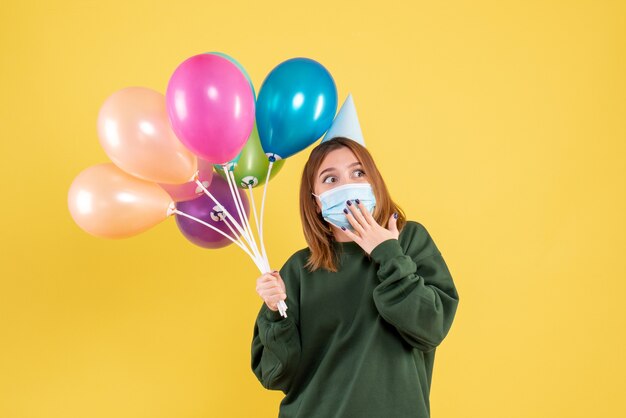 Vorderansicht junge Frau in der Maske, die bunte Luftballons hält