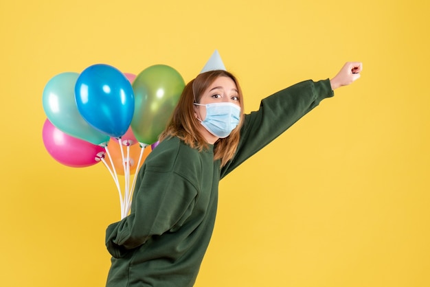 Vorderansicht junge Frau in der Maske, die bunte Luftballons hält