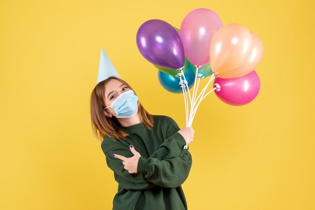 Vorderansicht junge Frau in der Maske, die bunte Luftballons hält