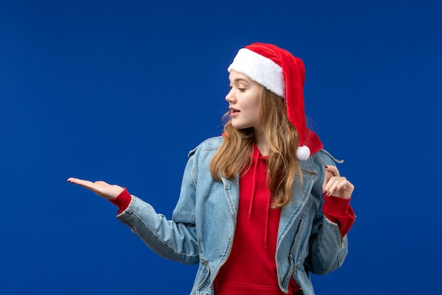Vorderansicht junge Frau in der roten Weihnachtskappe auf der Weihnachtshintergrund-Emotionsfarbe des blauen Hintergrunds