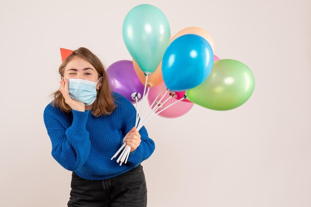 Vorderansicht junge Frau in der sterilen Maske, die bunte Luftballons hält