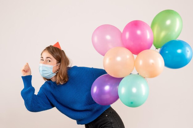 Vorderansicht junge Frau in der sterilen Maske, die bunte Luftballons hält