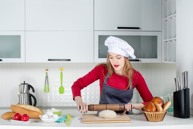 Vorderansicht junge Frau in Kochmütze und Schürze Teigrollen in der Küche