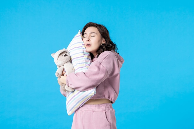 Vorderansicht junge Frau in rosa Pyjamas mit kleinem Spielzeugbär und Kissen auf blauem Bett Albtraum Schlaffrau Rest Schlaflosigkeit Traumparty