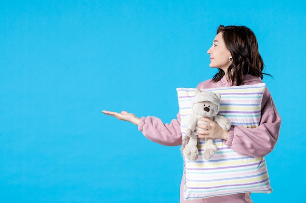 Vorderansicht junge Frau in rosa Pyjamas mit kleinem Spielzeugbär und Kissen auf blauem Schlaflosigkeitsfrauenbett Nacht Albtraum Traumparty Rest Schlaf