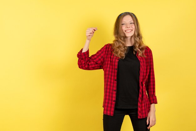 Vorderansicht junge Frau in rotem kariertem Hemd, das mit Lächeln auf gelbem Hintergrund menschliches Mädchen Emotionen Farbmodellfrau aufwirft