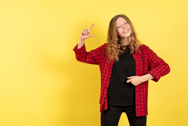 Vorderansicht junge Frau in rotem kariertem Hemd, das mit Lächeln auf gelbem Hintergrund menschliches Mädchenemotionsfarbmodellfrau aufwirft