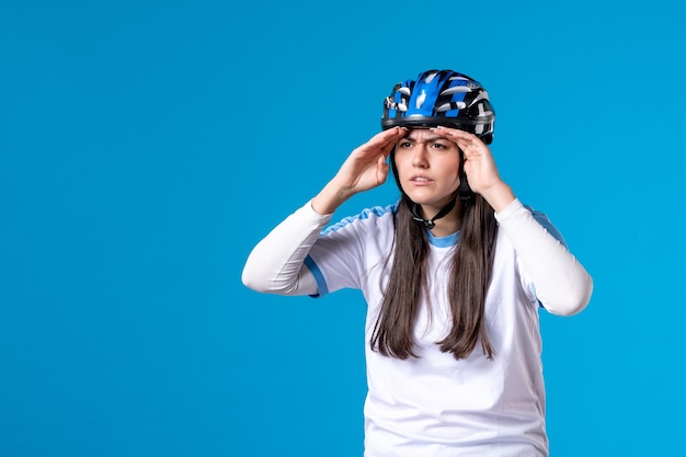 Kostenloses Foto vorderansicht junge frau in sportkleidung mit helm, der abstand auf blauer wand betrachtet