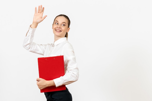 Vorderansicht junge Frau in weißer Bluse mit roter Datei in ihren Händen Gruß auf weißem Hintergrund Bürojob weibliche Emotion Gefühl Modell