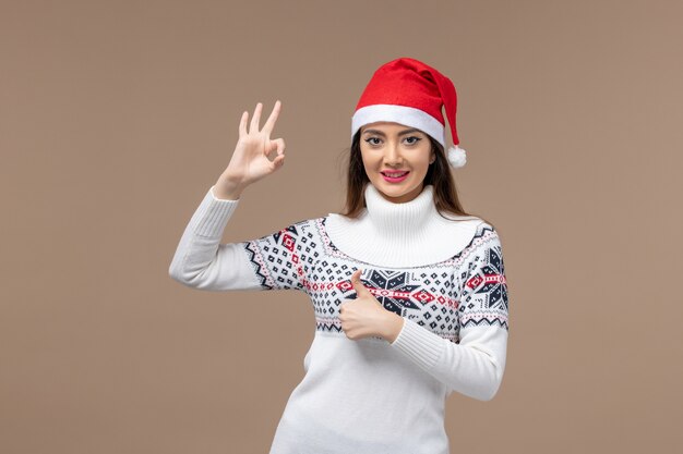 Vorderansicht junge Frau lächelnd mit roter Kappe auf braunem Hintergrund Emotion Weihnachten Neujahr