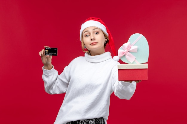 Vorderansicht junge Frau mit Bankkarte und Geschenken auf rotem Hintergrund