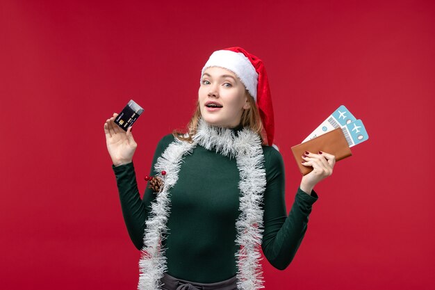 Vorderansicht junge Frau mit Bankkarte und Tickets auf rotem Hintergrund