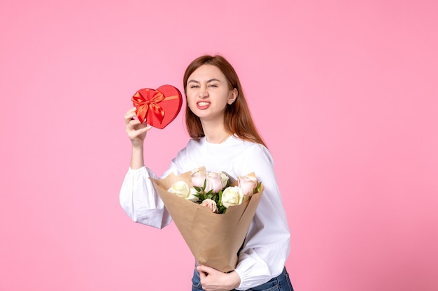 Vorderansicht junge frau mit blumen und geschenk als frauentag geschenk auf rosa hintergrund horizontale märz frau gleichheit liebe sinnliche datum rose