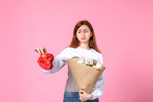 Vorderansicht junge Frau mit Blumen und Geschenk als Frauentag Geschenk auf rosa Hintergrund horizontale März Gleichheit sinnliche Datum Rose Frau Liebe