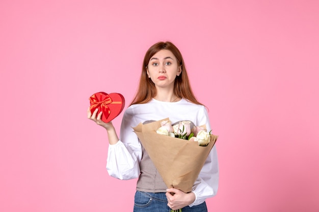 Vorderansicht junge Frau mit Blumen und Geschenk als Frauentagsgeschenk auf rosa Hintergrund horizontaler Marschgleichheit sinnliche weibliche Datumsfrau Liebe