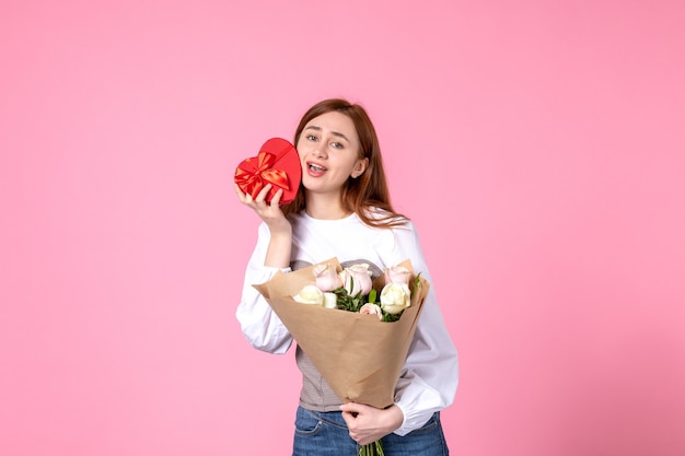 Vorderansicht junge Frau mit Blumen und Geschenk als Frauentagsgeschenk auf rosa Hintergrund horizontaler Marschgleichheit weibliches Datum Rosen Frau Liebe sinnlich