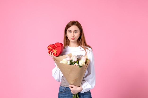 Vorderansicht junge Frau mit Blumen und Geschenk als Frauentagsgeschenk auf rosa Hintergrund stieg horizontaler Marsch weibliches Datum weibliche Liebesliebe Gleichheit