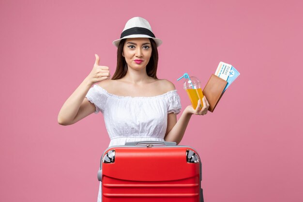 Vorderansicht junge Frau mit Flugtickets für Urlaub und Saft auf der rosa Wand Sommerreise Emotion Flugzeug Reise