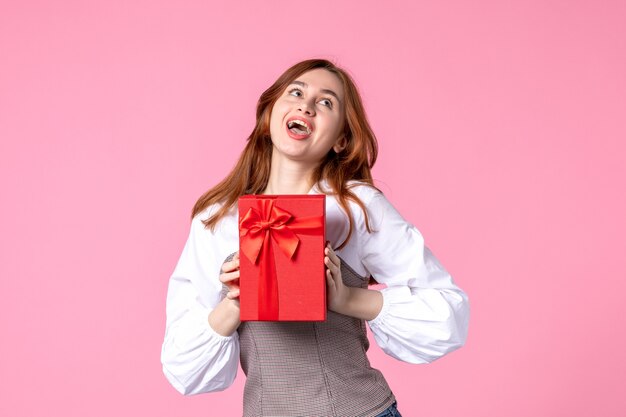 Vorderansicht junge Frau mit Geschenk im roten Paket auf rosa Hintergrund Liebesdatum März horizontale sinnliche Geschenk Parfüm Foto Geld Gleichheit