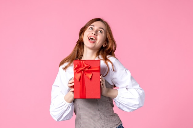 Vorderansicht junge Frau mit Geschenk im roten Paket auf rosa Hintergrund Liebesdatum März horizontale sinnliche Geschenk Parfüm Foto Geld Gleichheit