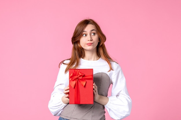 Vorderansicht junge Frau mit Geschenk im roten Paket auf rosa Hintergrund Liebesdatum März horizontale sinnliche Parfüm Frau Foto Geld Gleichheit