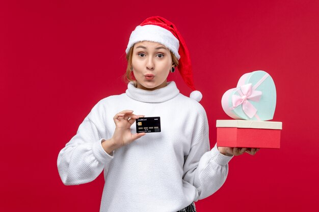 Vorderansicht junge Frau mit Geschenken und Bankkarte auf dem roten Hintergrund