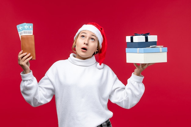 Vorderansicht junge Frau mit Geschenken und Tickets auf einem roten Hintergrund