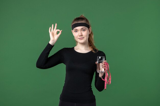 Vorderansicht junge Frau mit Glas Wasser und Taillenmaß auf Grün