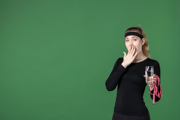 Vorderansicht junge Frau mit Glas Wasser und Taillenmaß auf grünem Hintergrund Farbe Gesundheit Körper schwarze Sportlerin Sport