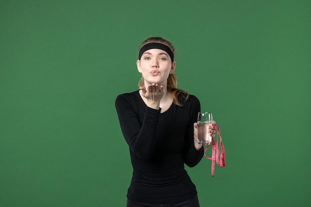 Vorderansicht junge Frau mit Glas Wasser und Taillenmaß auf grünem Hintergrund Gesundheit Sport Athlet Frau Farbe schwarz Training