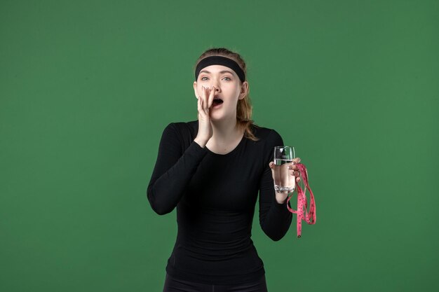 Vorderansicht junge Frau mit Glas Wasser und Taillenmaß auf grünem Hintergrund Gesundheit Sport Athlet Körper schwarze Trainingsfarbe Frau
