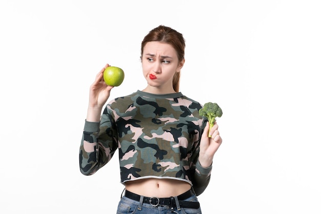 Vorderansicht junge Frau mit grünem Apfel und kleinem Brokkoli auf weißem Hintergrund Haut Wellness horizontaler Gesundheitssaft menschliche Frucht